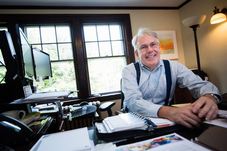 Silver-haired man smiles happily at a desk