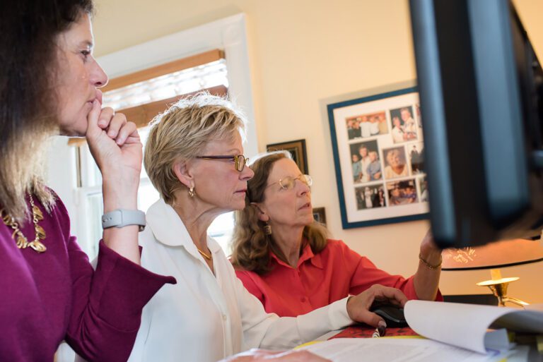 Three well-dressed female employees discussing the data pulled up on a computer screen