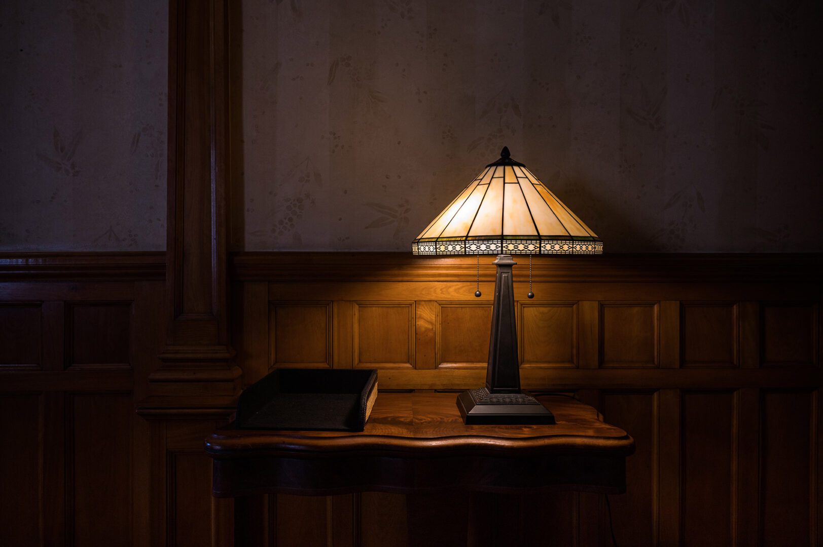 Stained glass lamp glowing with warm-colored light in dark room with wood paneling